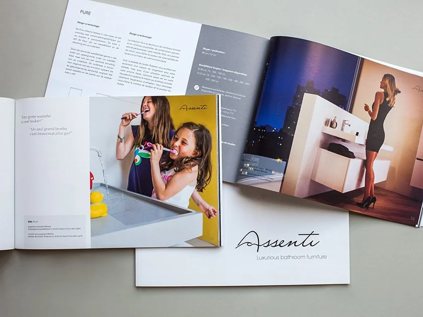 Open brochure featuring images of modern bathroom designs, including a bathroom with a woman in a black dress and high heels, and children brushing their teeth, with a city skyline visible in the background.
