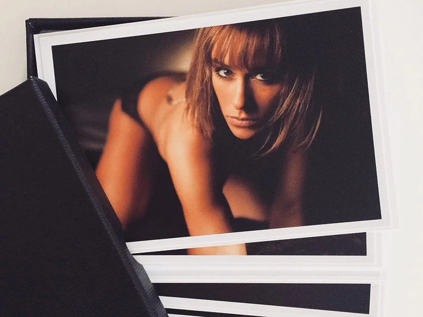 Printed photograph of a woman with brown hair looking directly at the camera, partially obscured by a black zipped case.