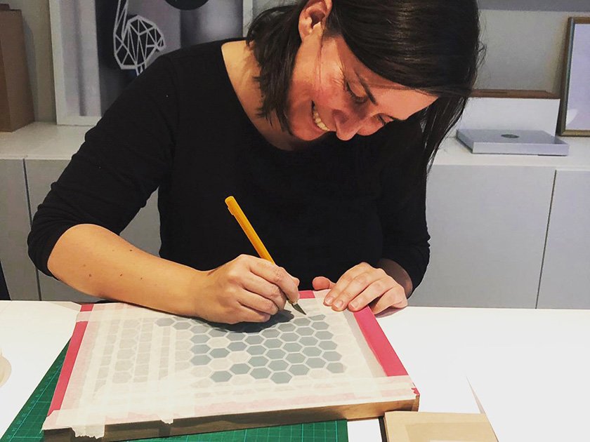 Woman smiling and marking a grid of hexagon patterns on a board with a yellow marker.