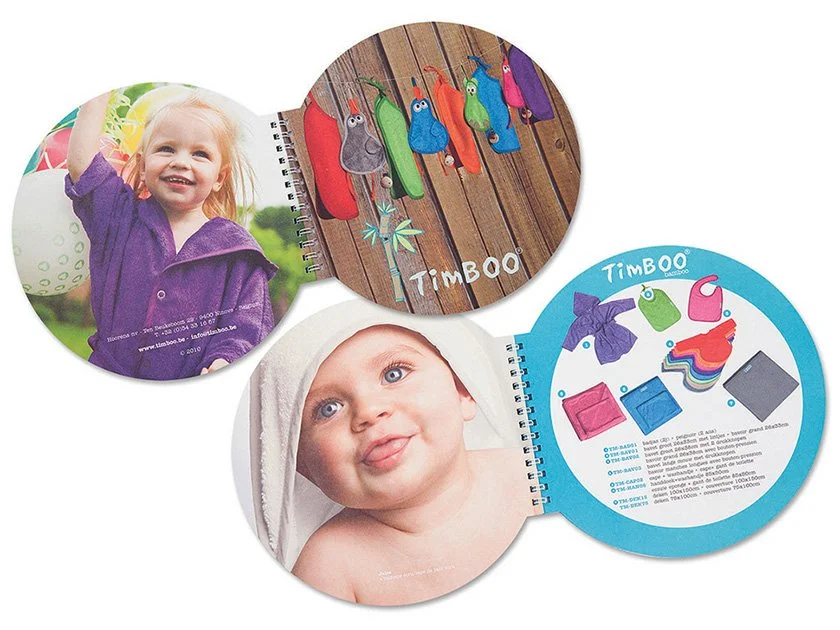 Three open circular pages from a children's photo album, featuring a girl smiling outdoors, a baby with a towel on their head making a funny face, and colorful toy animals and accessories with branding 'TimbO'.