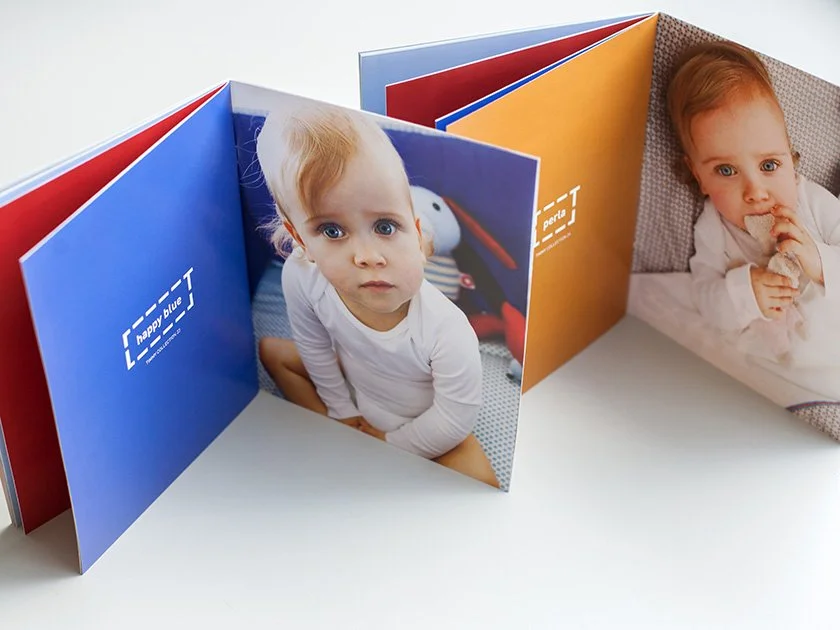 Open photo book showing two pages with images of young children, one with a girl and the other with a toddler, on a white surface background.