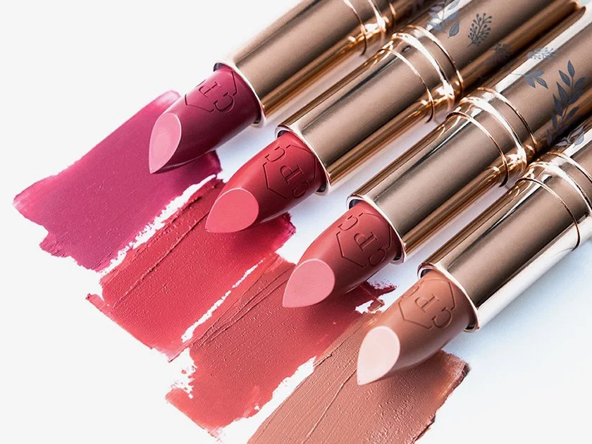 Four lipsticks in shades of pink and nude with swatches of their colors on a white surface.