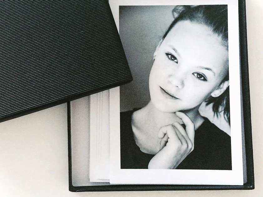Black and white portrait of a woman with her hand resting near her face inside a photo album.