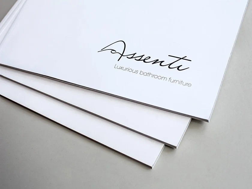 Brochures or catalogs with the brand name 'Assenti' and the tagline 'Luxurious bathroom furniture' on the cover, stacked on a white surface.