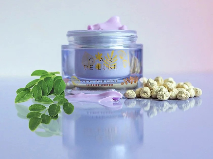 A skincare product jar with pink cream on top, green leaves on the left, white chickpeas on the right, and a soft pastel background.