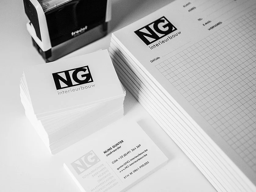 Business cards, a stack of printed sheets, and a printing machine on a desk.