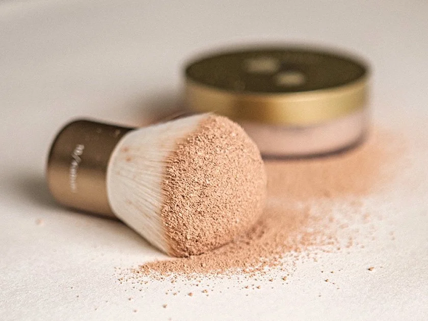 Cosmetic brush with loose powder and a compact powder container on a white surface.
