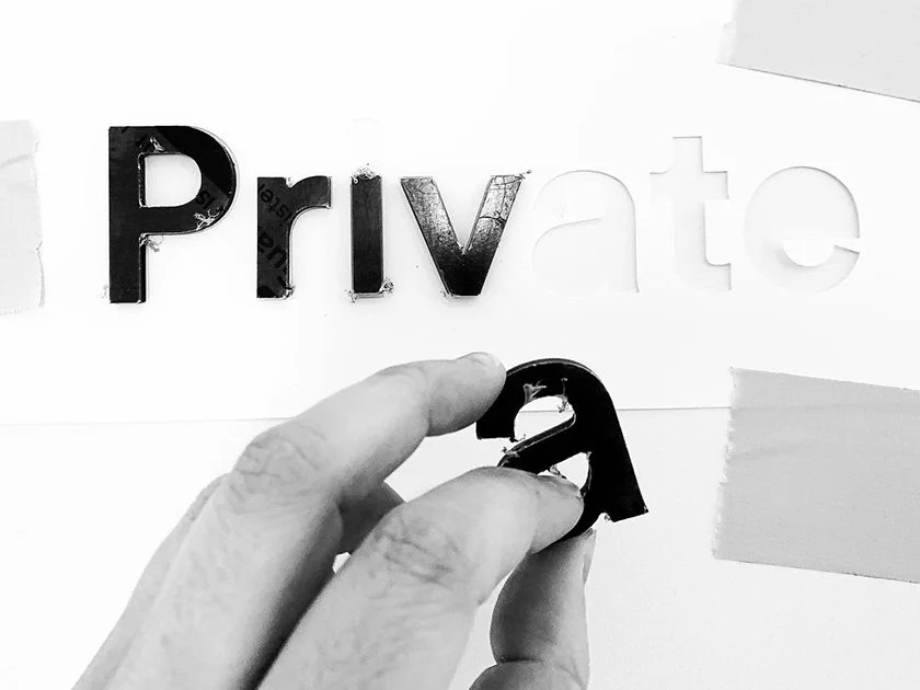 Hand holding a black letter 'A' in front of cut-out letters spelling 'Private' on a white background.