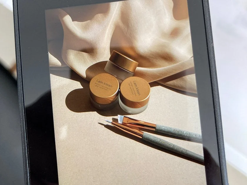 Three small jars labeled 'I am. Klean' and two makeup brushes on a beige fabric background and surface.