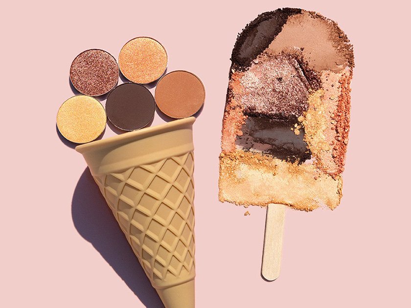 An ice cream cone with five different eyeshadow pans and a makeup sponge painted to look like a popsicle with a colorful, textured pattern.