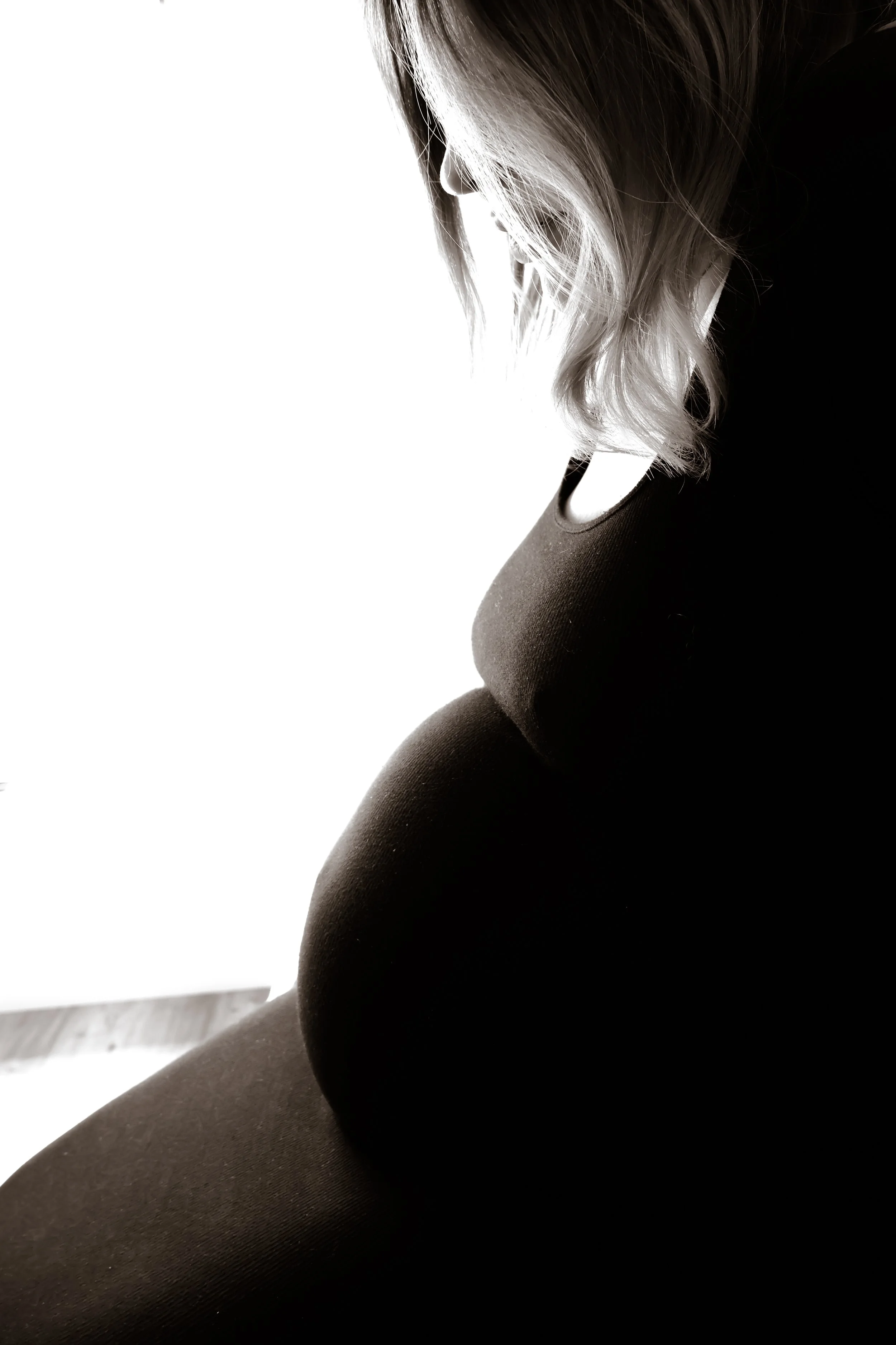 Black and white photo of pregnant woman with long hair, sitting and looking downward.