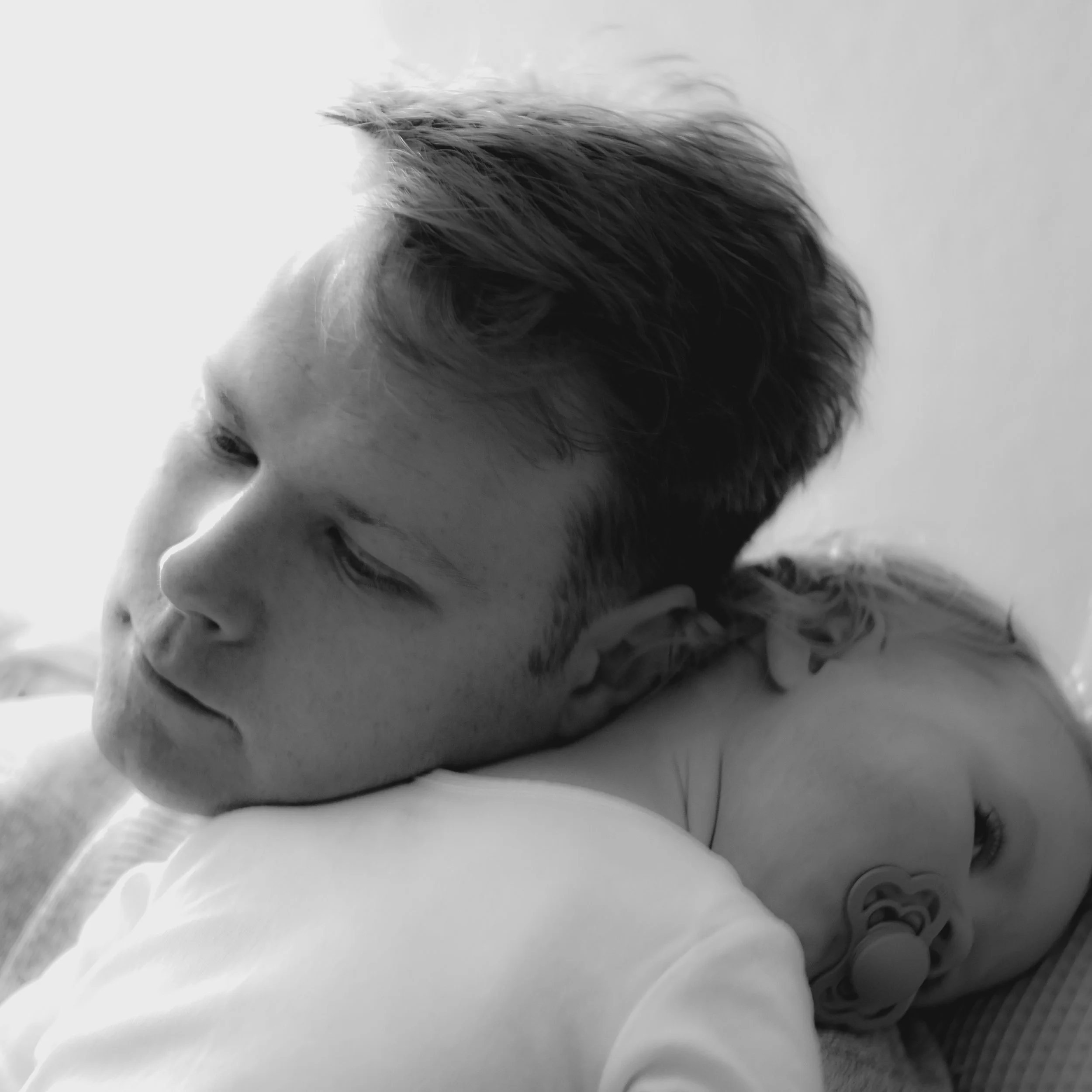 A young man resting his head on a pillow, with a baby lying next to him, both appearing peaceful.