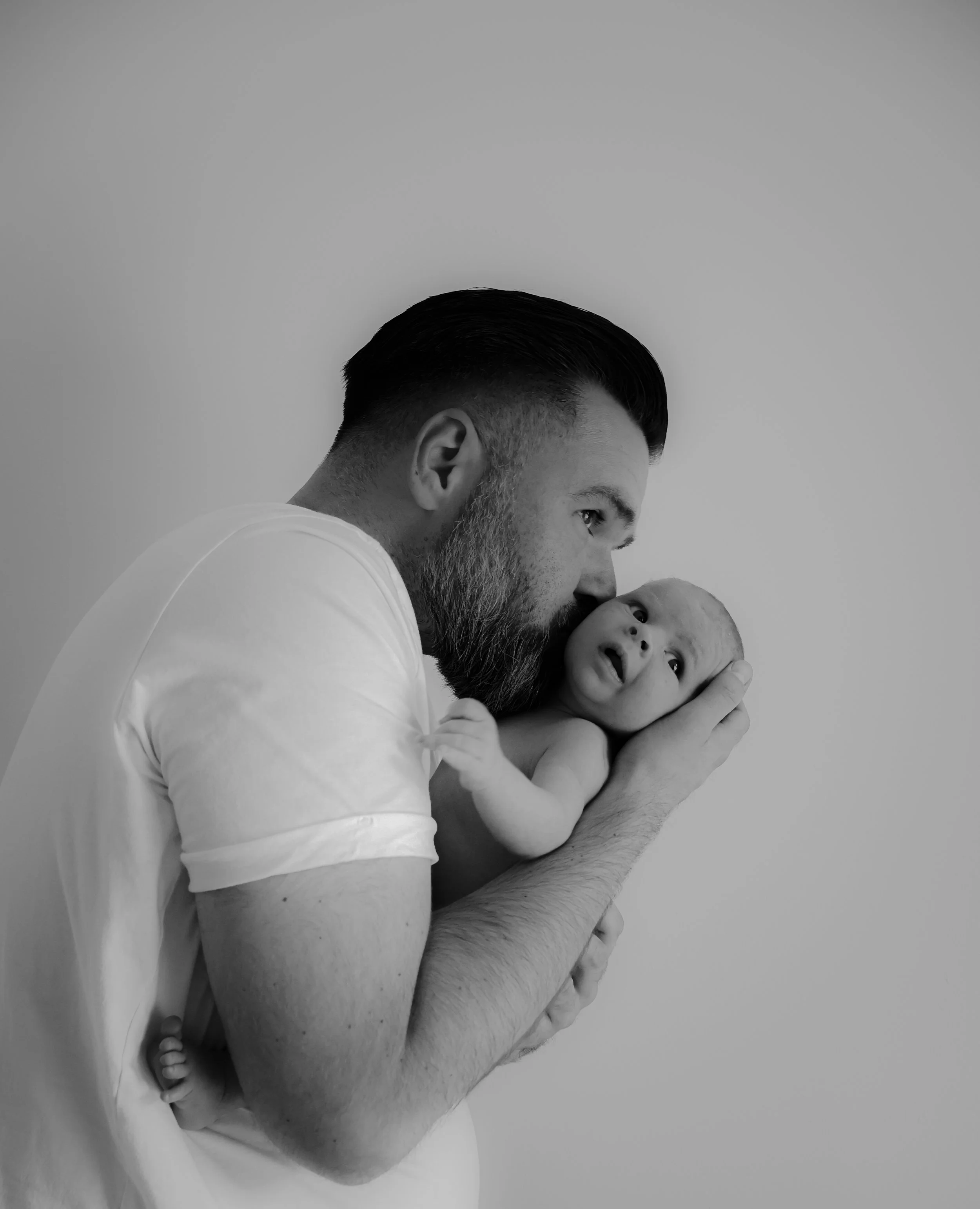 A man holding a baby close to his face, appearing to kiss or nuzzle the baby's head. The image is in black and white.