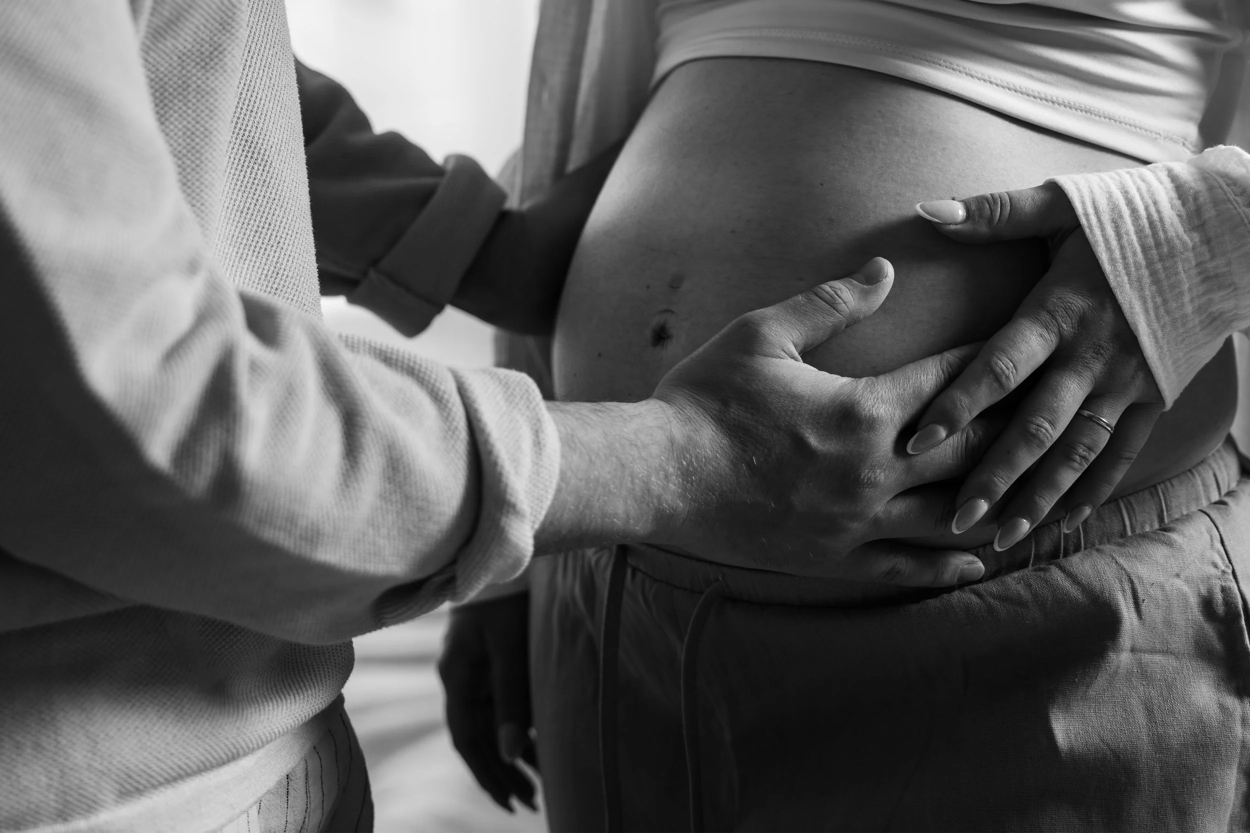 Nahaufnahme von zwei Personen, die sich an den Bauch fassen, im schwarz-weiß. Eine Person hält den Bauch einer anderen Person, vermutlich in der Schwangerschaft.