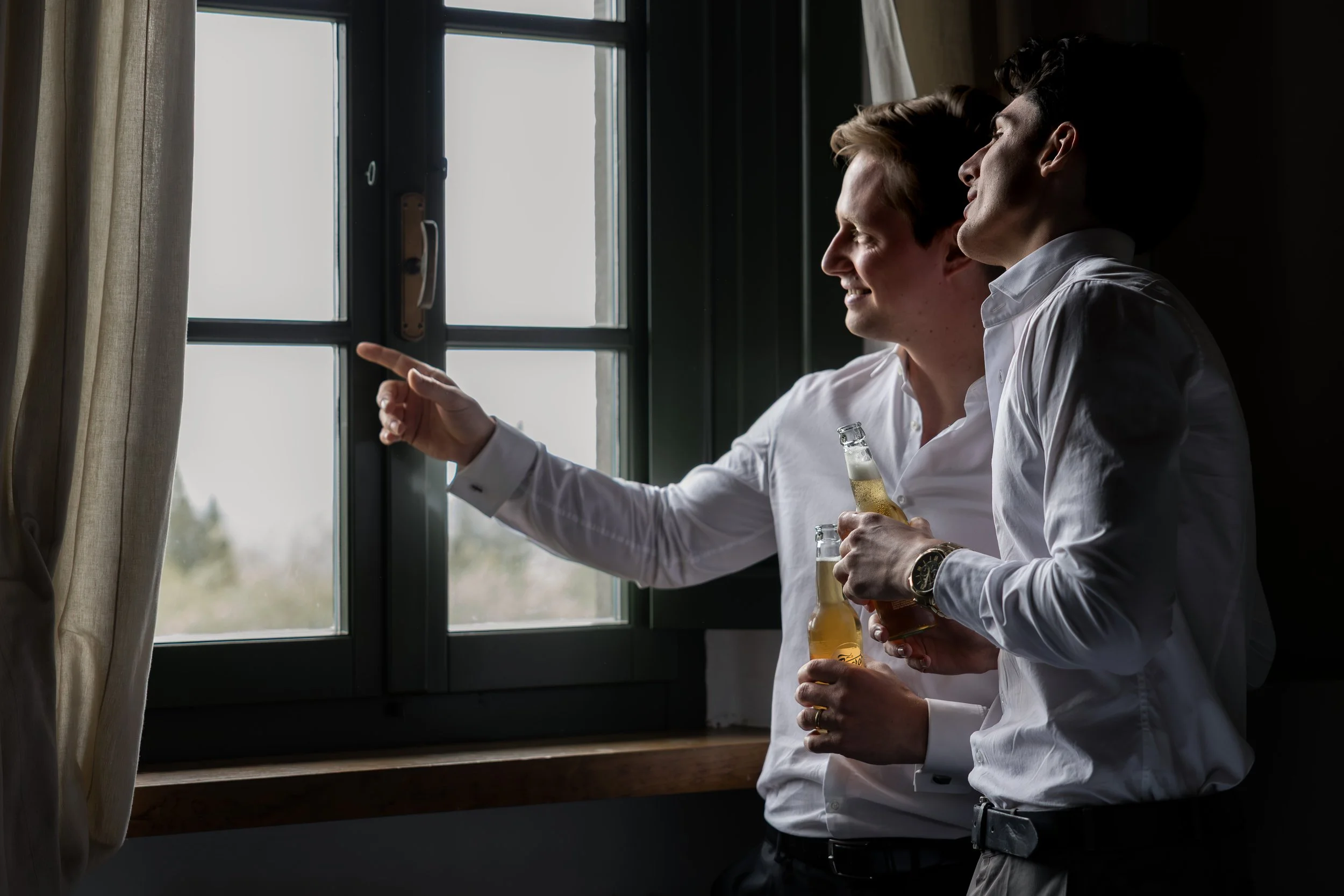 Zwei Bräutigame während des Getting Ready am Fenster vor ihrer Hochzeit.