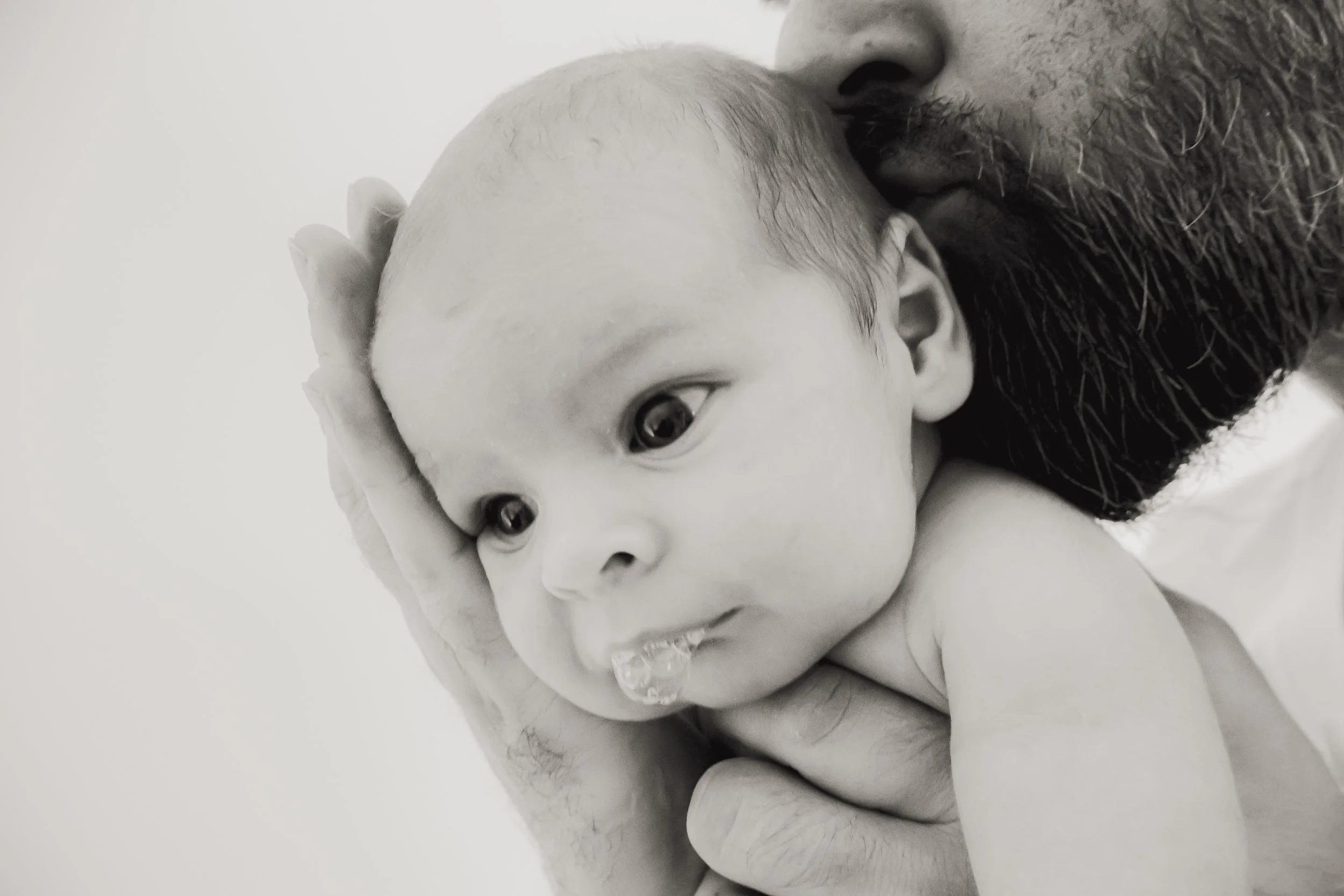 A man gently holding and kissing a baby on the head, with the baby's face close to the camera, in black and white.