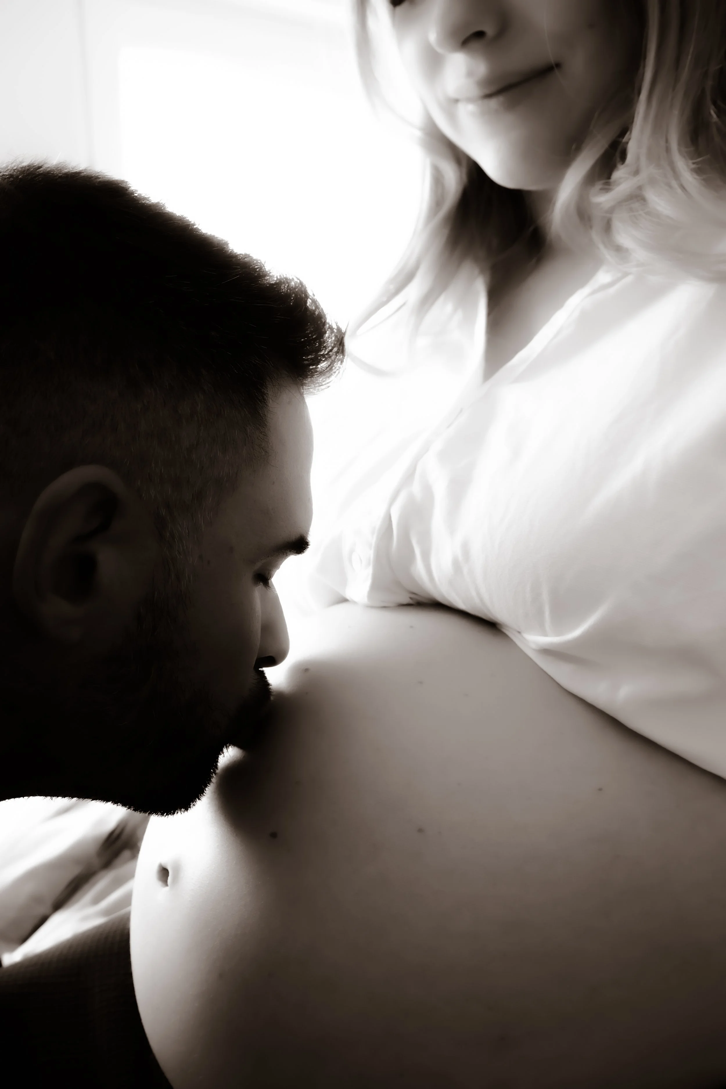 A man kissing a pregnant woman's belly in a close-up black-and-white photo.