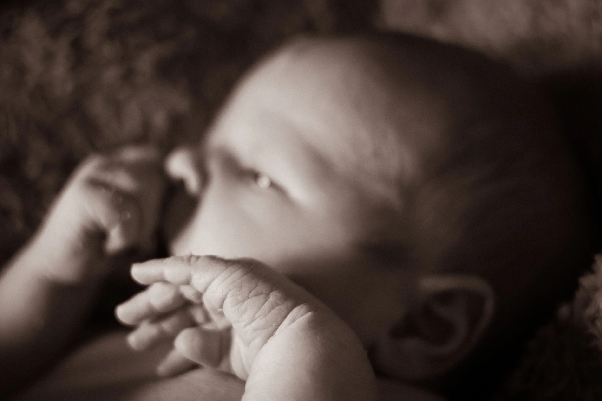 A close-up of a sleeping baby lying on a soft surface, with one hand near its face and the other arm resting by its side.