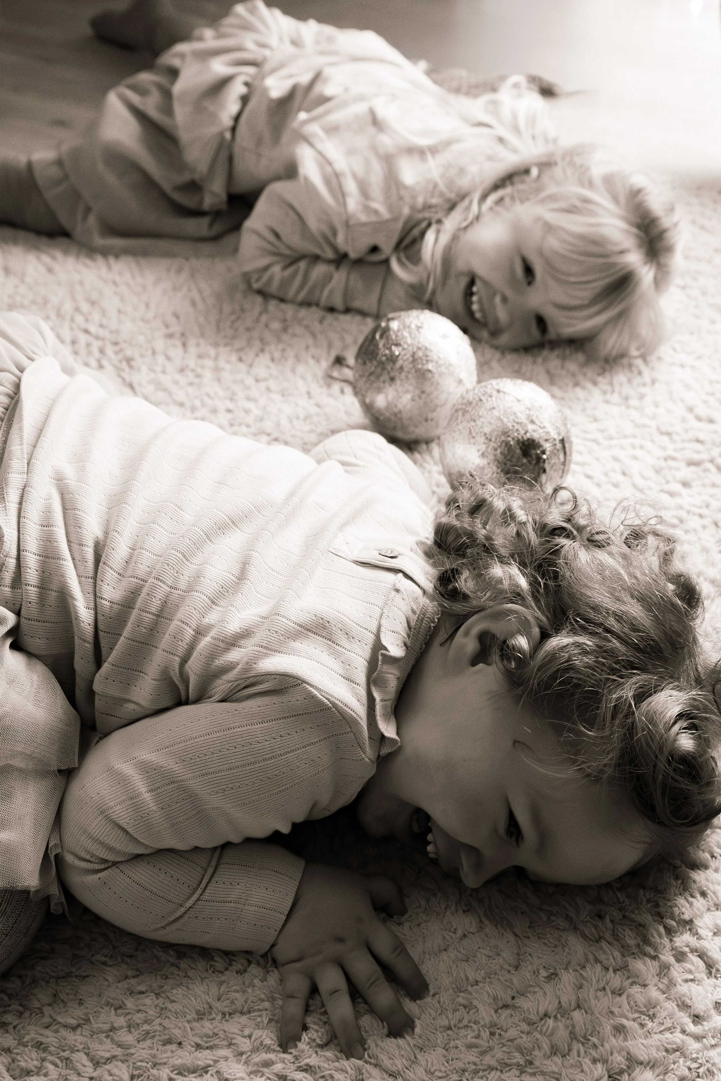 Two children lying on a carpeted floor, smiling and playing with decorative spheres.