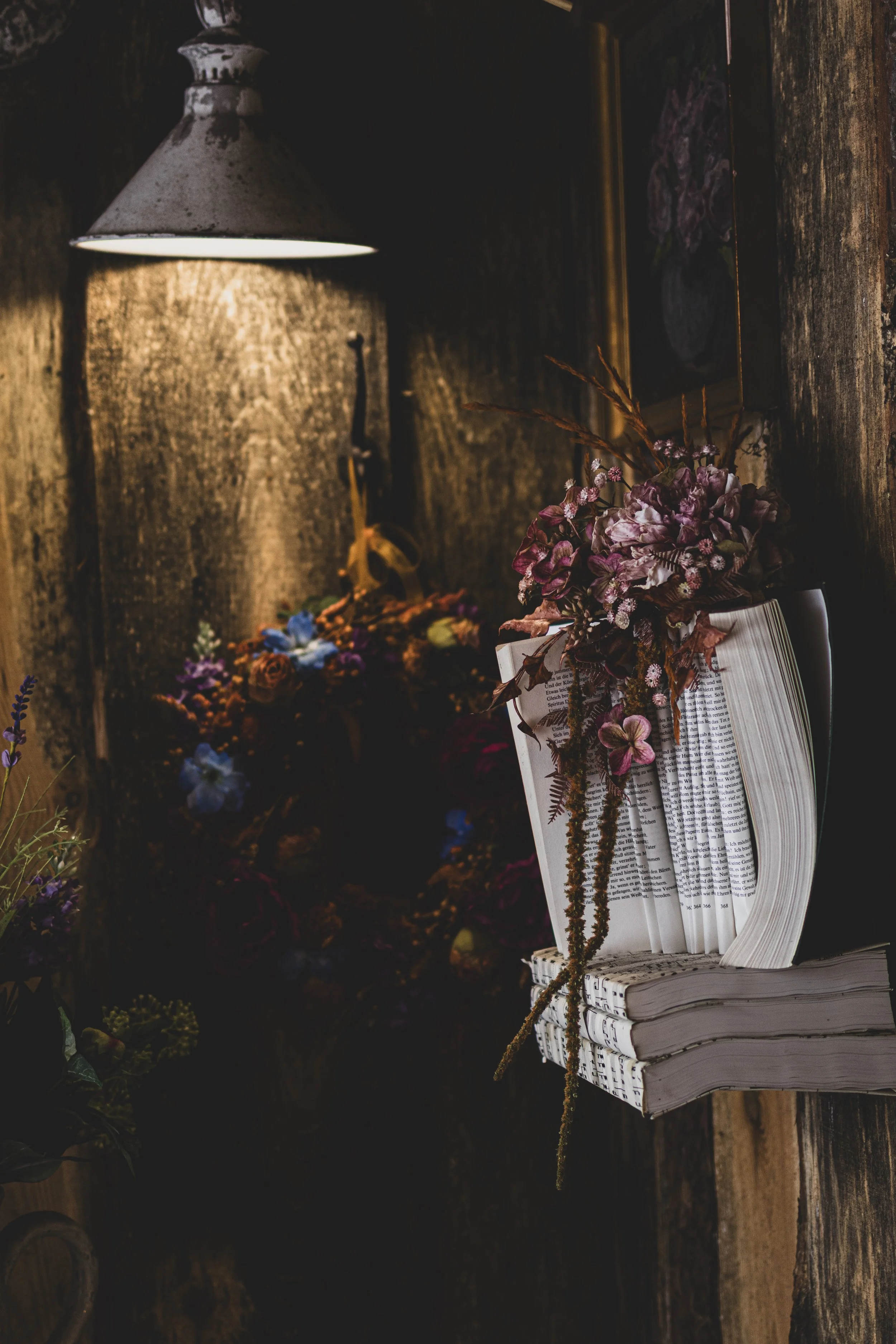 Ein aufgeschlagenes Buch mit Blumenicker auf einem alten Holzstuhl, in einem rustikalen Raum mit dunklen Holzwänden und Blumen im Hintergrund, beleuchtet von einer alten Metalllampe.
