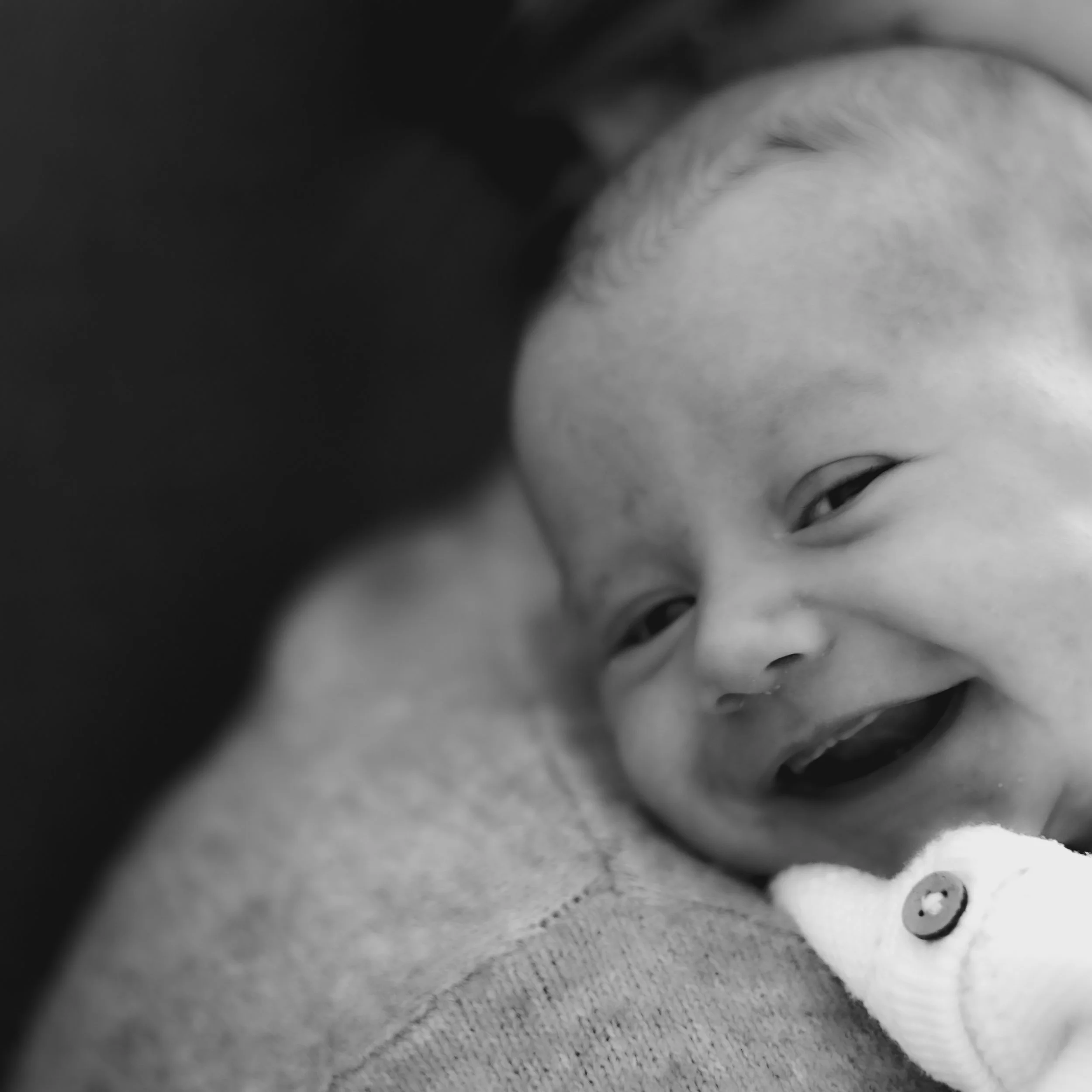 A close-up black and white photo of a smiling baby with a joyful expression, lying on a soft surface.