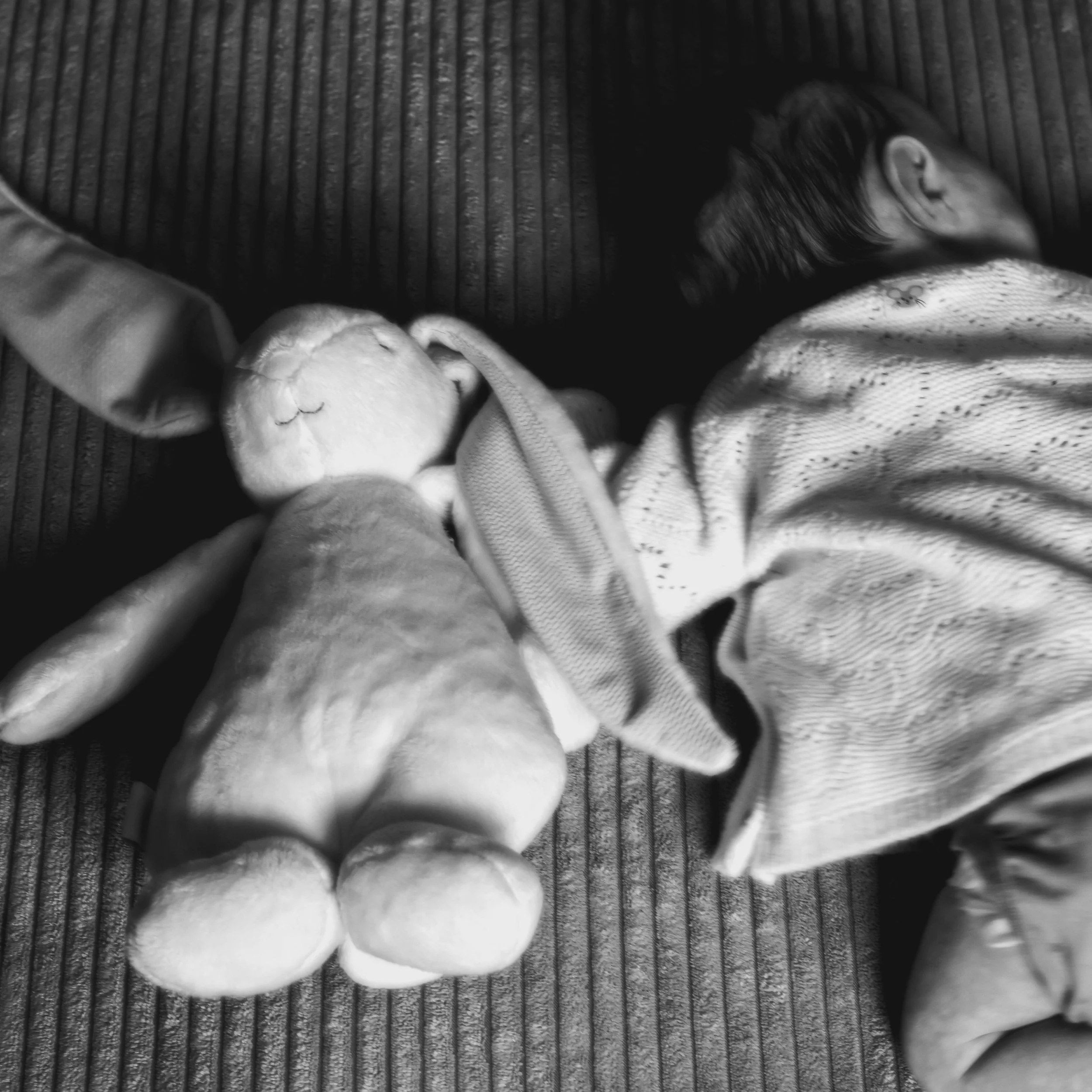 A child lying on a striped fabric surface, sleeping with a stuffed animal held in one hand.
