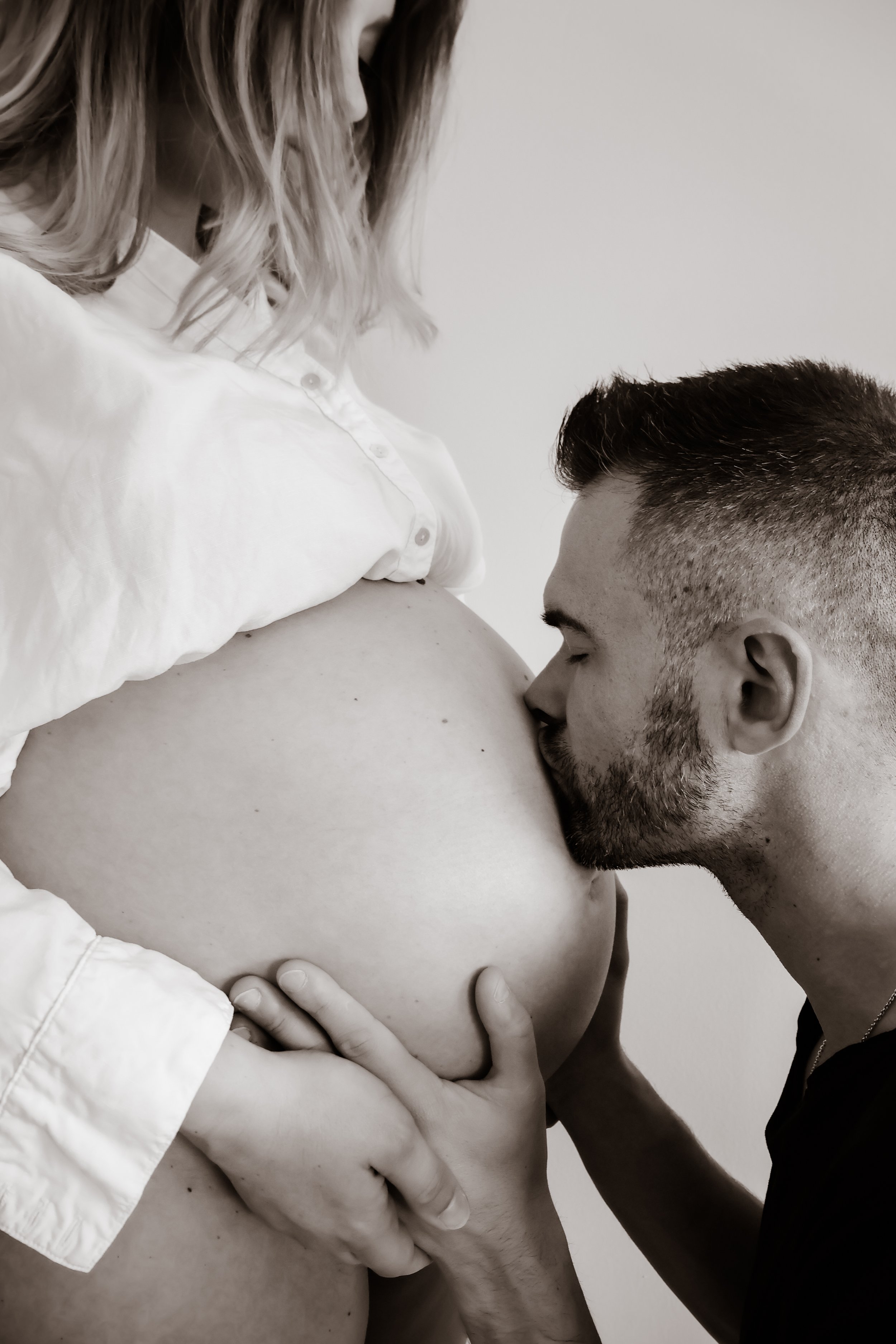 A man kissed a pregnant woman's belly while holding her waist, with his eyes closed, in black and white.