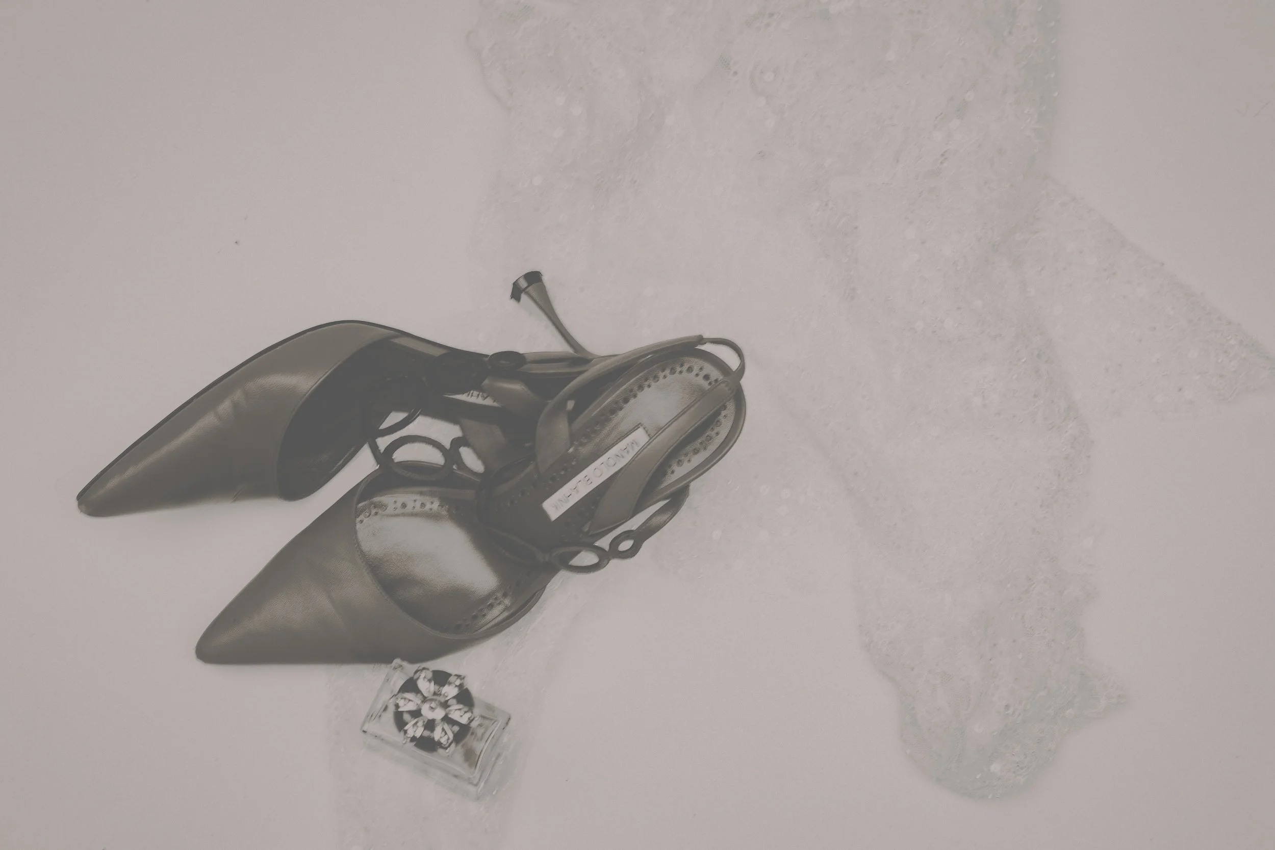 Silver high-heeled shoes, a small perfume bottle, and a diver's helmet are arranged on white foam and partially submerged in bubbles and foam.