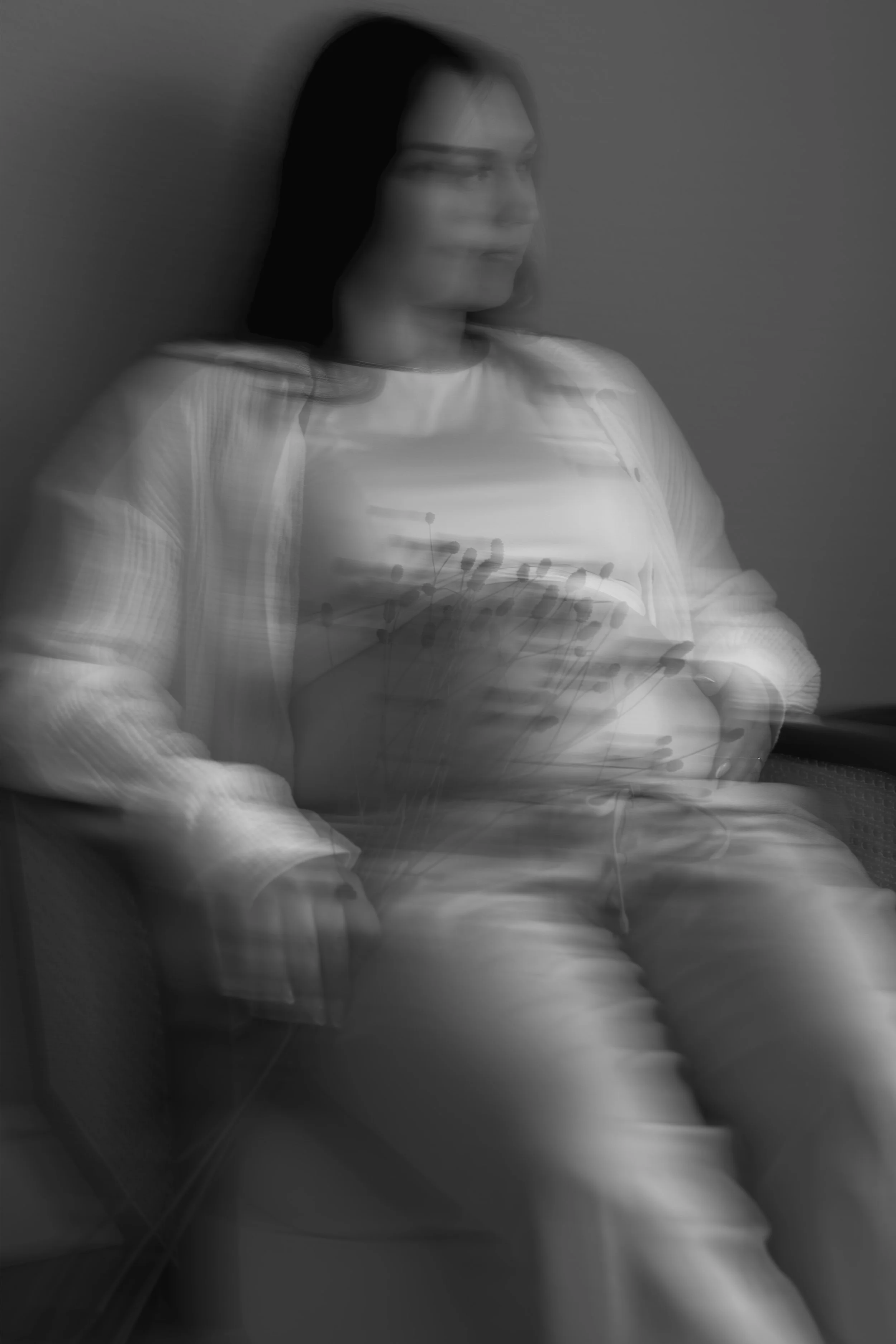 Schwarz-weiß-Bild einer Frau mit langen dunklen Haaren, die nach rechts schaut. Sie trägt ein helles Oberteil; der Hintergrund ist grau. Das Bild hat einen verschwommenen Effekt.