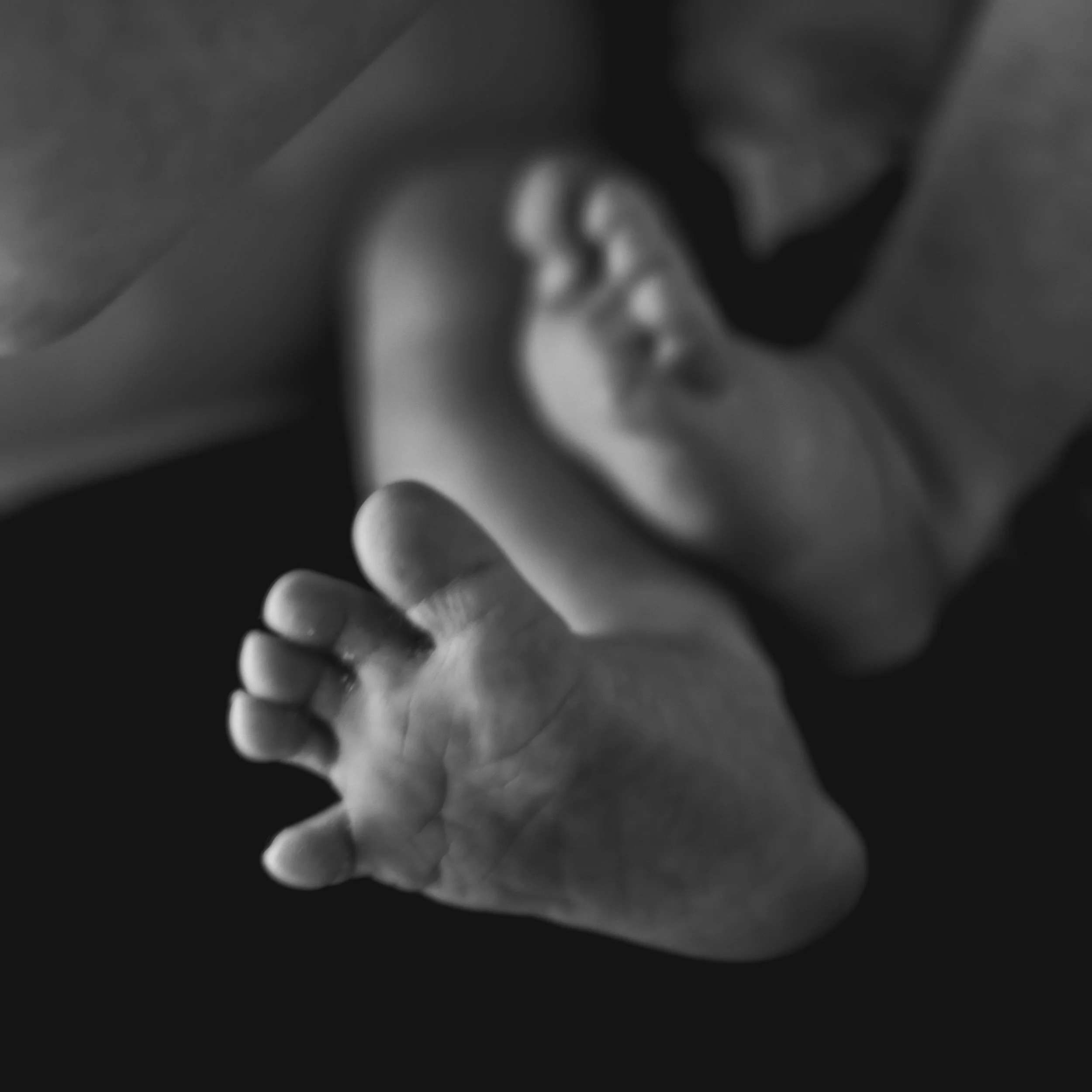 Black and white photo of a baby's hand reaching out with a blurred face of the baby in the background.