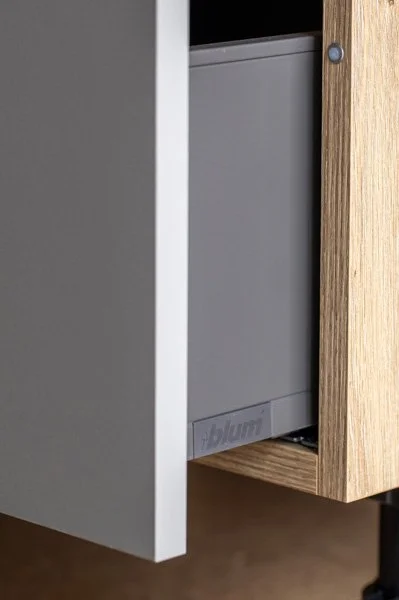 Close-up of a gray metal Blum drawer partially open inside a wooden cabinet.