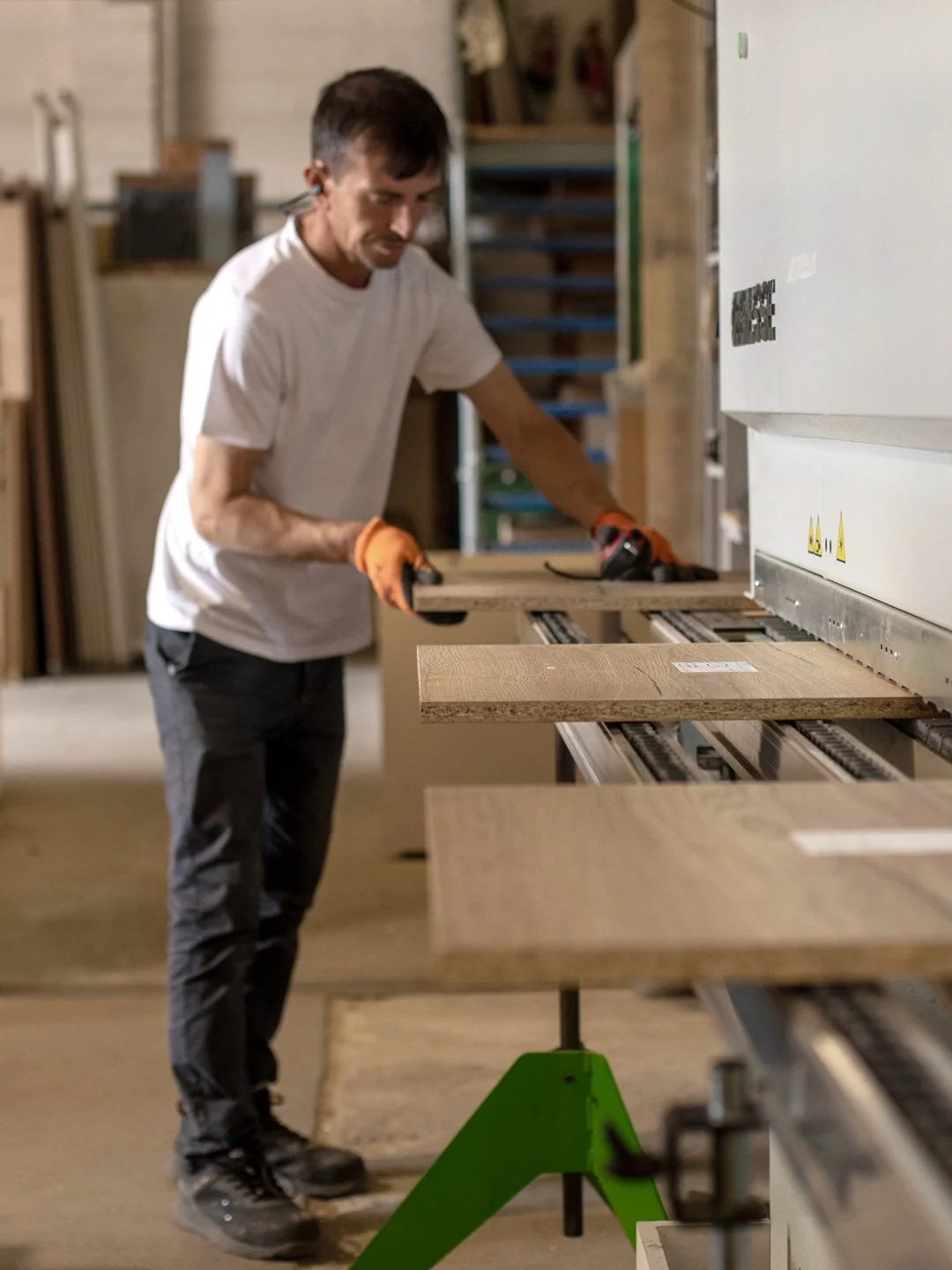 A man working in a woodworking shop, placing a wooden plank into a machine for cutting or shaping.