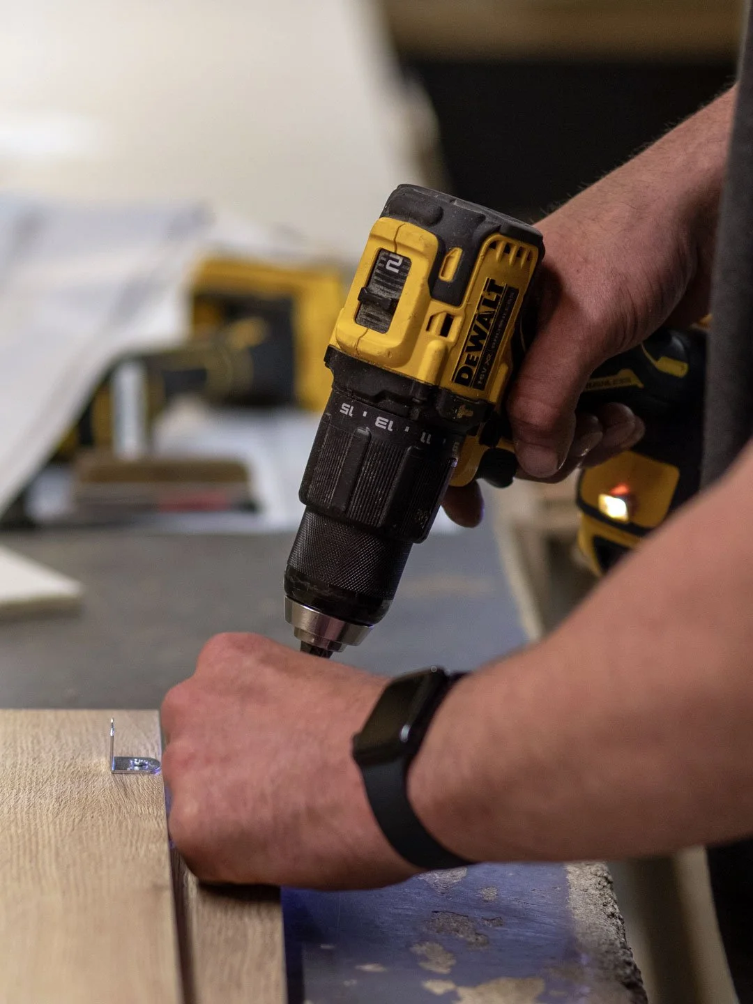Person using a yellow DeWalt cordless drill to attach a screw into a wooden surface.