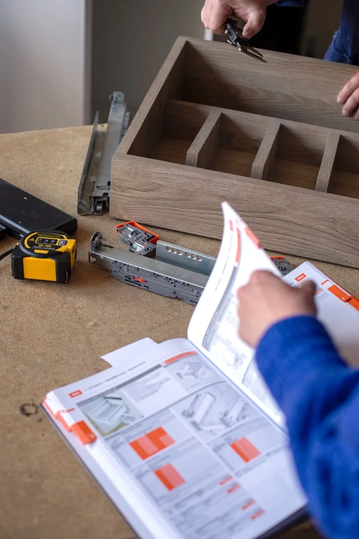 A person working on assembling a wooden drawer, with tools and instruction manuals on a workbench.