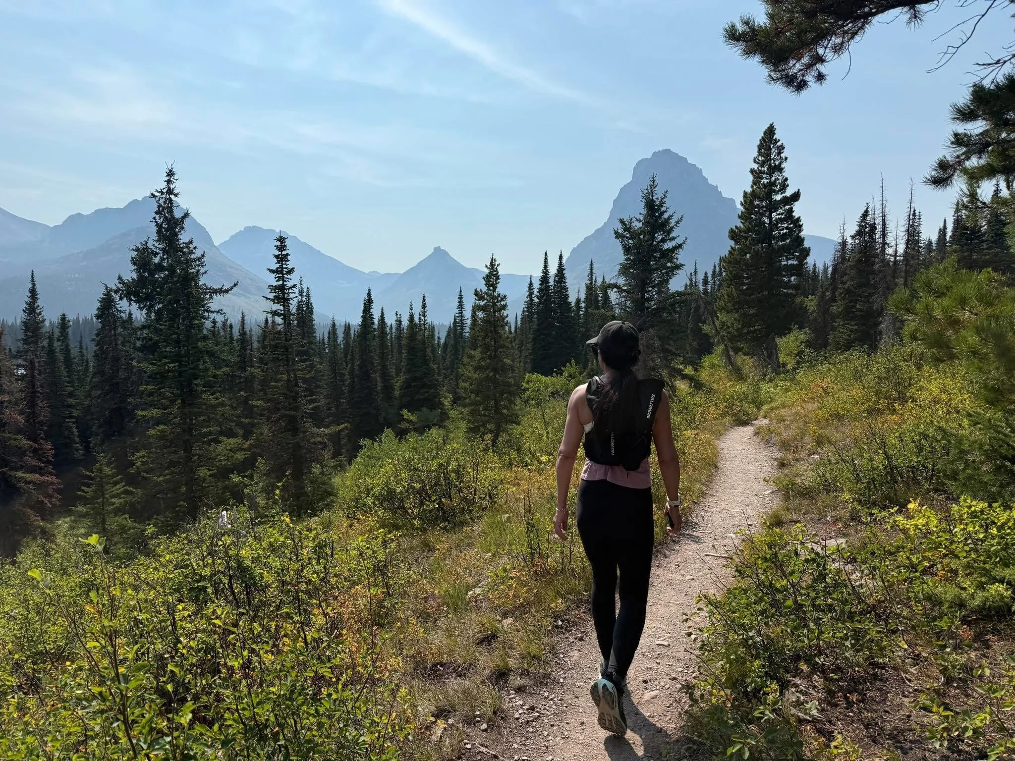 A woman hiking on a trail through a mountainous forest landscape.