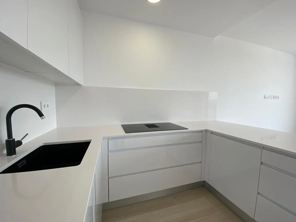 Cocina moderna con gabinetes blancos y encimera blanca, fregadero negro y grifo negro, estufa de inducción negra.