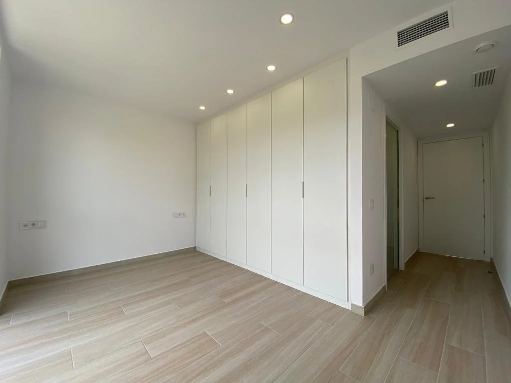 Habitación vacía con paredes blancas, suelo de madera y armario empotrado blanco, con varias luces empotradas en el techo.