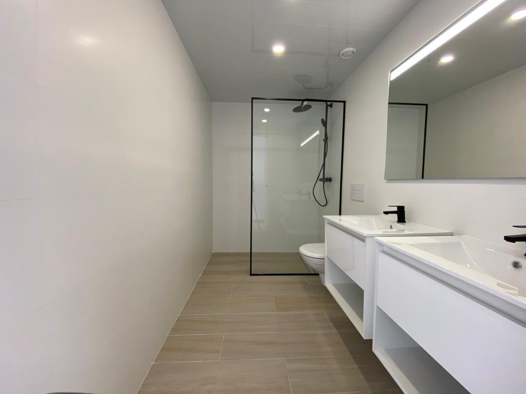 Baño moderno con ducha, inodorito y doble lavabo con espejo grande