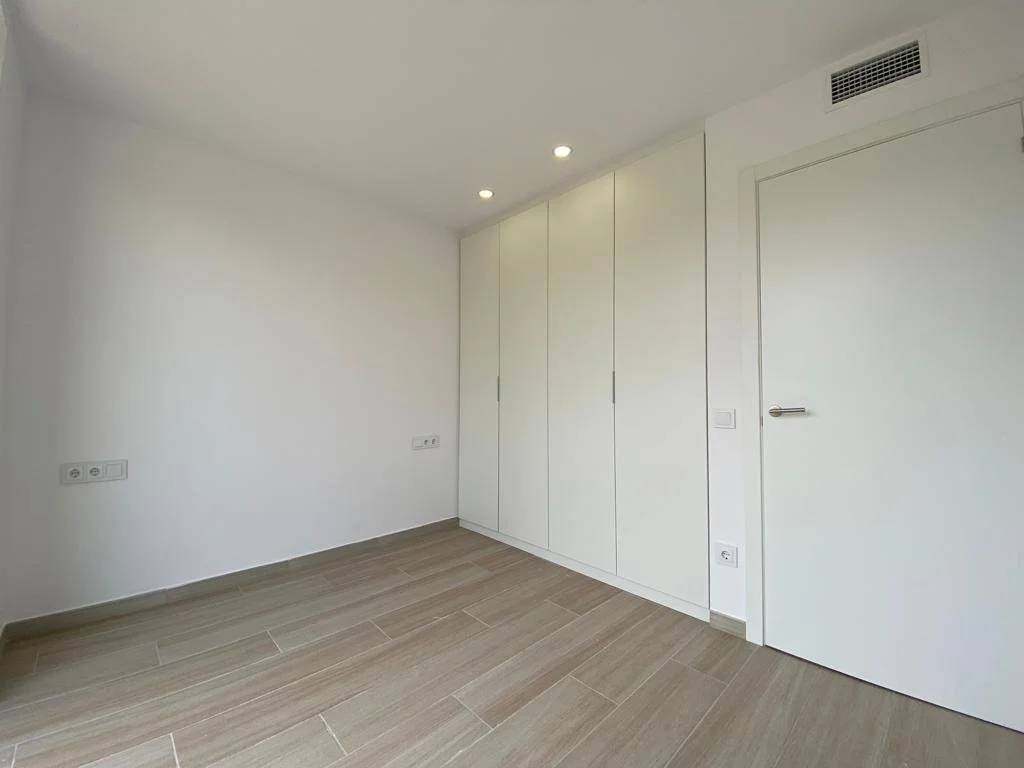 Cuarto vacío con paredes blancas, piso de madera clara, armario empotrado con puertas blancas y techo con luces empotradas.