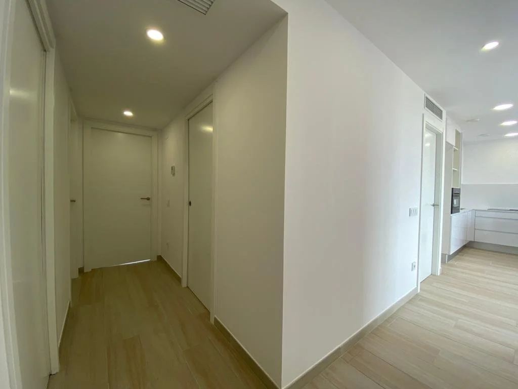 Pasillo con puertas blancas y piso de madera, en un espacio de vivienda moderna con iluminación empotrada en el techo.