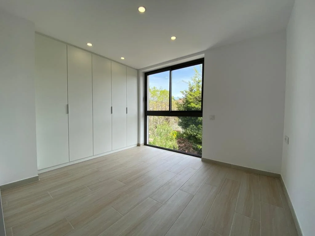 Habitación vacía con armario empotrado, ventana grande y suelo de madera clara.