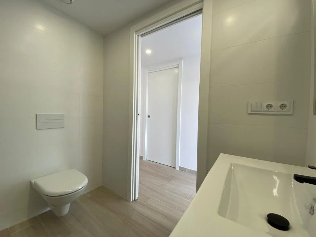 Inodoro y lavabo en un baño con paredes blancas y piso de madera clara