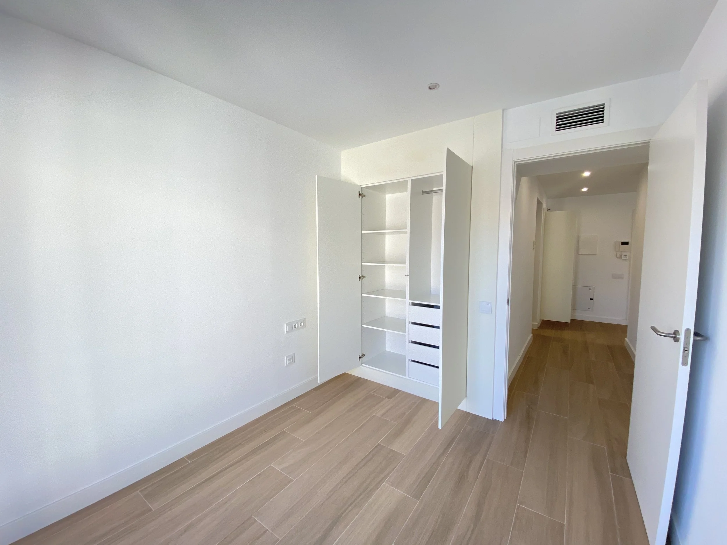 Habitación vacía con paredes blancas, suelo de madera y armario empotrado abierto.