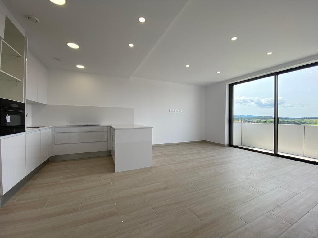 Sala vacía con cocina moderna, grandes ventanas y vista panorámica desde el balcón.