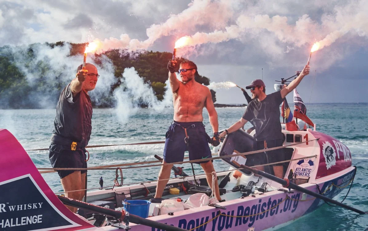 Team Margot each holding a lit flare emitting smoke, celebrating on the water after finishing the World's Toughest Row