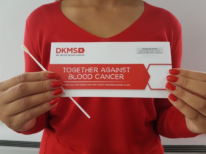 Person holding a blood donation ticket for DKMS Blood Cancer organization, wearing a red shirt with matching red nail polish.