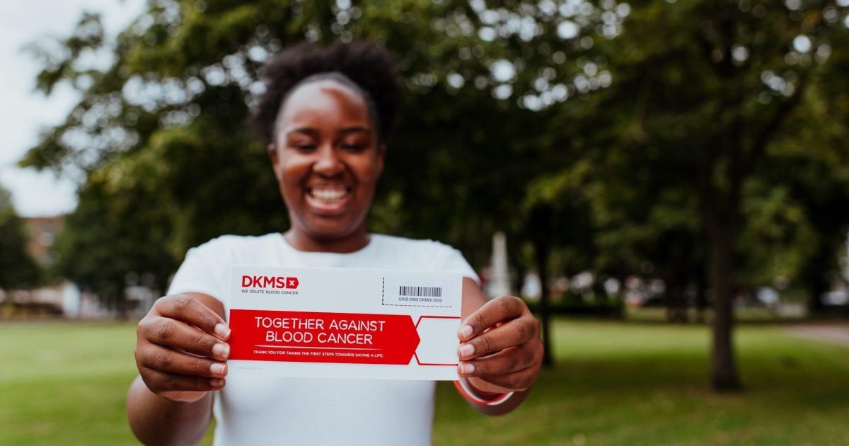 Woman smiling outdoors holding a blood donation form that says "Together Against Blood Cancer".