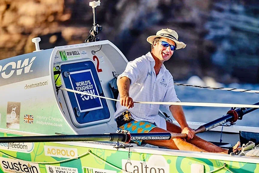  Henry Cheape with short curly hair wearing sunglasses, a wide-brim hat, a white polo shirt, and colourful shorts, finishes the World's Toughest Row