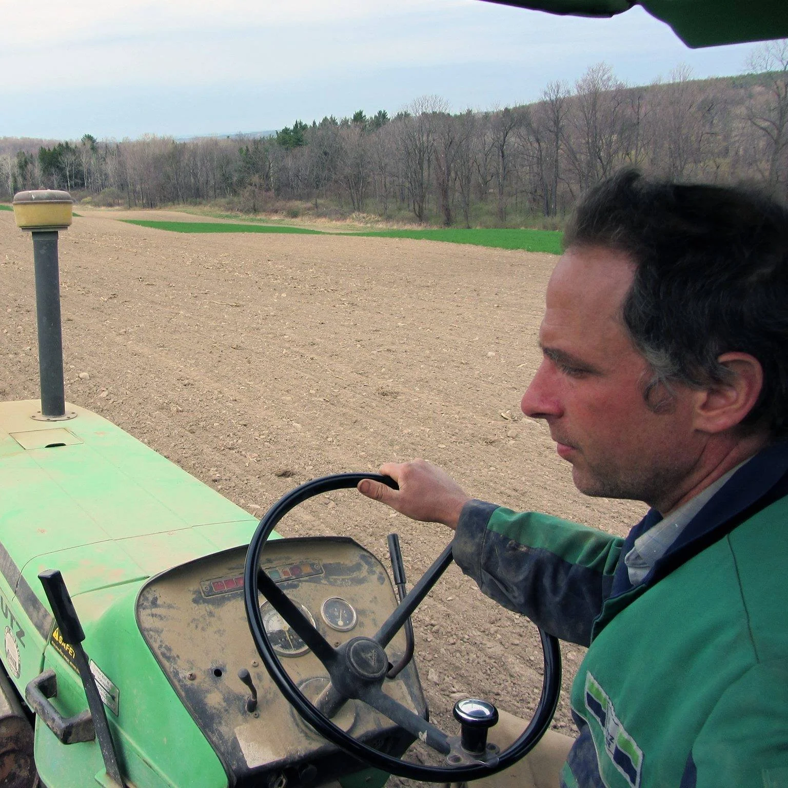 A man driving a green tractor across a farm field with a tractor dashboard visible.