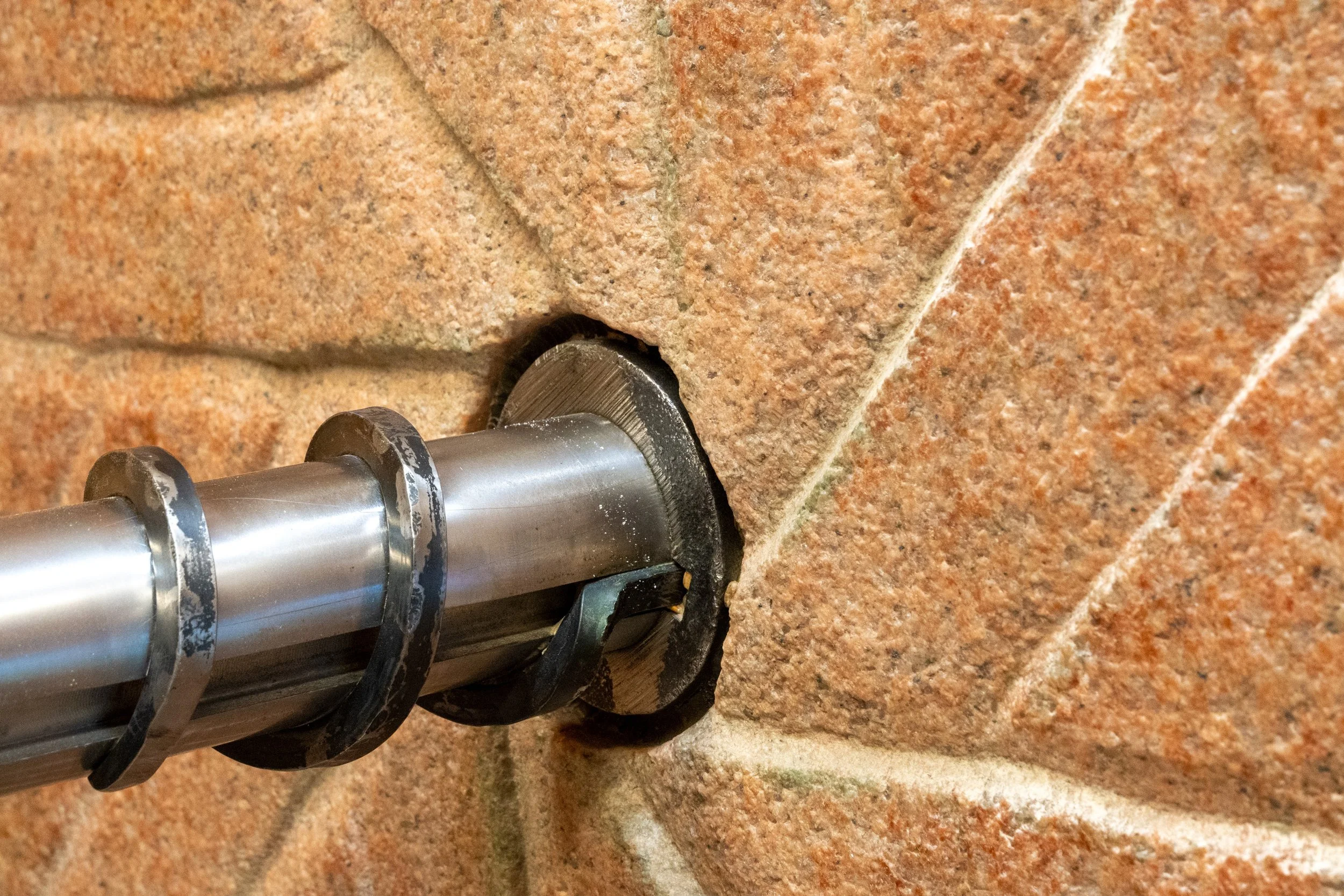 Close-up view a mill stone made from pink granite. Clearly shown are the furrows that have been chiseled into the stone for grain movement. Going into the middle of the millstone is a steel shaft.